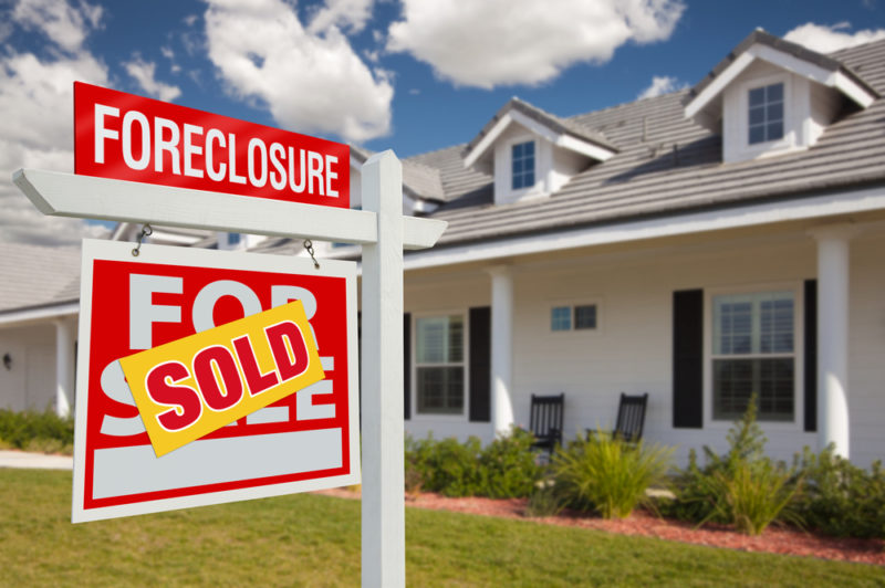 House with a foreclosure for sale sign, covered with a “sold” sticker.