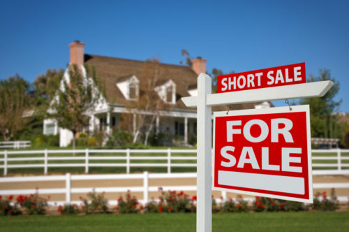 A house with a for sale sign in front, announcing a short sale
