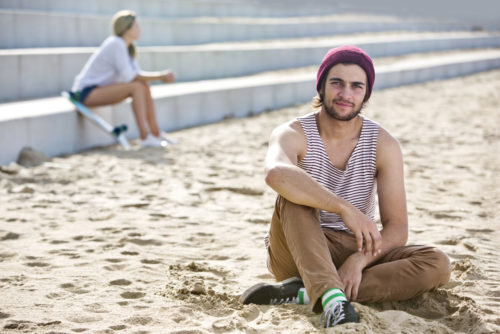 Teenage boy sitting in the sand with a young woman sitting on cement steps behind him