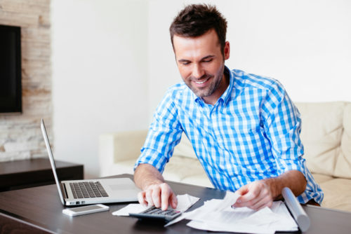 Smiling young man analyzing his expenses and using an online check cashing service