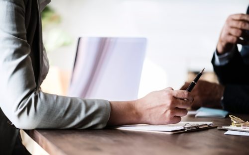 An individual with a pen and a clipboard speaking with another individual