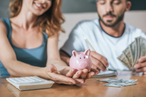 Couple planning family budget and holding piggy bank in living room.
