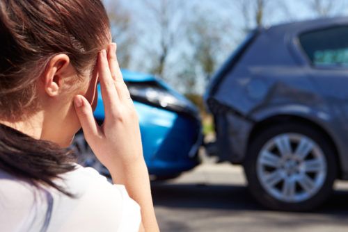 Woman holds head in front of car accident