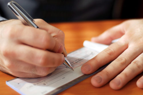 A man holding a pen over his checkbook, about to fill out a personal check.