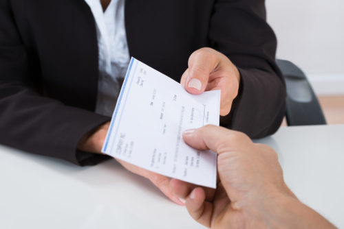 Closeup of a businessperson in a suit handing a paycheck over a desk to an employee.