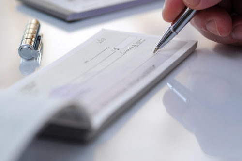 Close up of a person holding a pen over a check, prepared to fill it out.