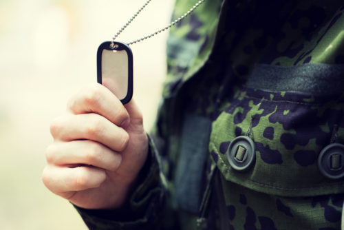Close up of a person in a camouflage uniform, holding an empty dog tag in their hand.