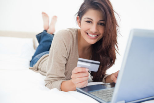 Woman smiling and looking ahead as she uses a laptop with a credit card in her hand.