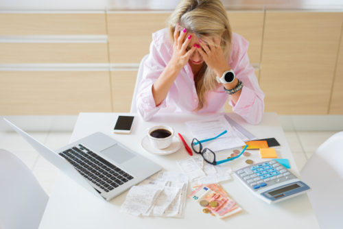 A woman sitting at her cluttered desk stresses over late payments and overdue bills