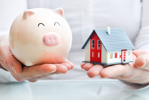 Hands holding a piggy bank and a model of a house