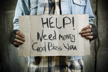 A man in a denim jacket, holding a sign that reads: “Help! Need Money. God Bless You.”