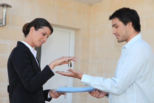 A woman hands a man keys while he hands her paperwork.