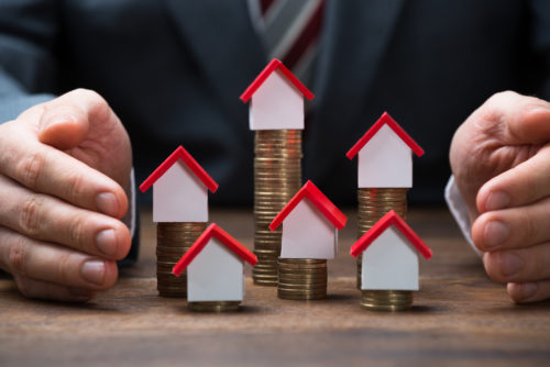 Businessman covering stacked coins with models of houses on a table