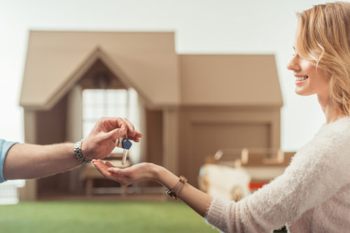 Woman receiving house keys from real estate agent in front of her new home.