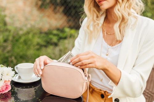 Image of a woman taking dollar banknotes out of her purse at a table in a cafe.