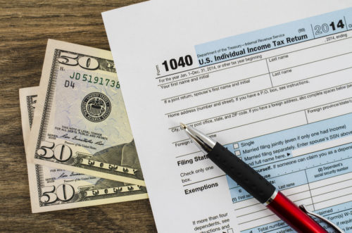 Two fifty dollar bills beneath a 1040 IRS income tax return form