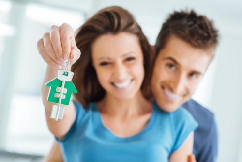 Happy young couple holding up a key and house keychain.