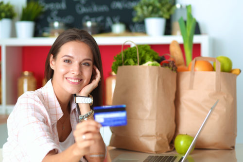 Smiling woman holding credit card with groceries behind her