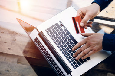 Someone types on a silver laptop while holding a red credit card