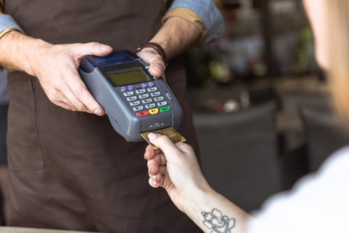 A photo of a waiter holding out a card reader while the customer inserts their card, chip first, into the reader.