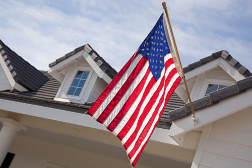 An American flag is hung in front of a home with a blue sky in the background.