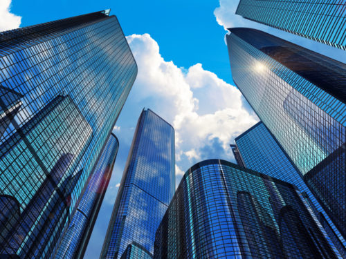 Ground level perspective looking up at modern office buildings against a blue sky