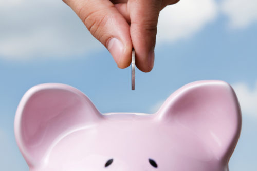 A closeup of someone’s fingertips as they put a coin into a piggy bank