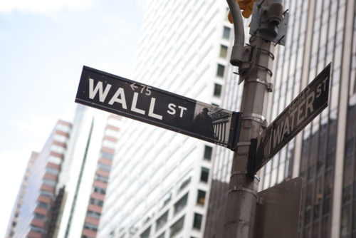 Street sign at the corner of Wall Street and Water Street against city backdrop.