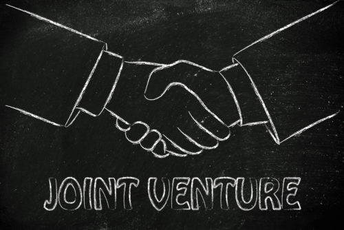 A sketch of hands shaking outlined in white on a black background, with the words “JOINT VENTURE” underneath.