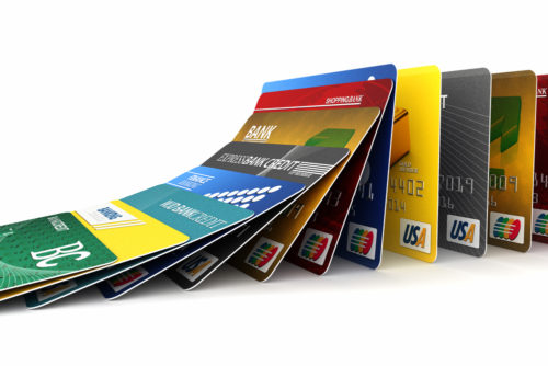 A photo of credit cards lined up in a row, toppling over like dominos in front of a white background.