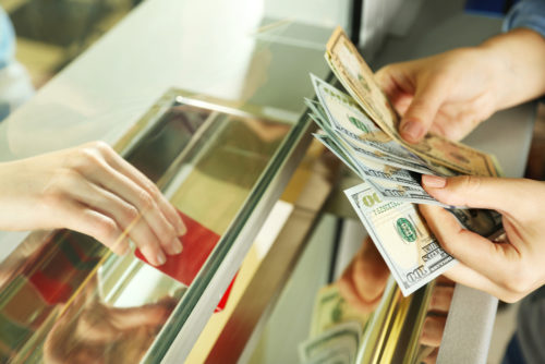 A bank teller counting out money behind safety glass while a customer hands over their card.