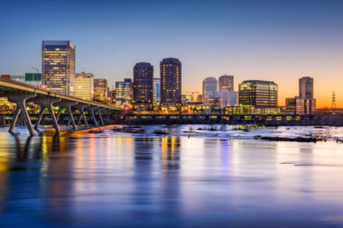 A skyline of Richmond, Virginia at sunset, shot from across the James River, with the Manchester bridge to the left of the frame.