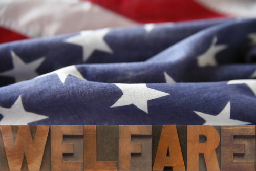 A photo of block letters saying “welfare” in front of an American flag.