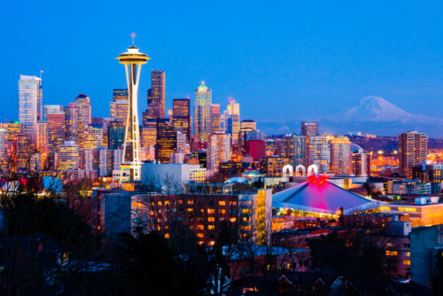 Panorama of downtown Seattle, Washington from a distance at night with buildings lighted up and Mount Rainier in background.