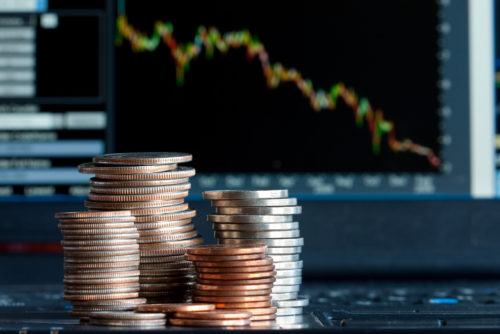 An image of a laptop screen displaying a financial graph with a downward trend. Stacks of small change appear in the foreground.