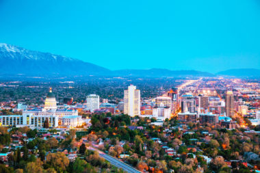 A landscape photograph of Salt Lake City from above, with foggy mountains and a blue sky in the background.