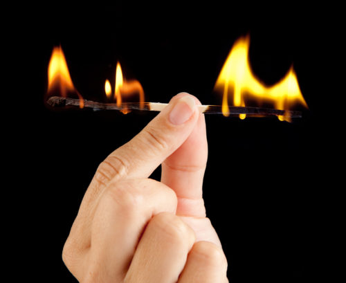 An image of a hand holding a match, which is burning at both ends as a metaphor for psychological burnout symptoms.