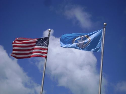 The United States and the Commonwealth of the Northern Mariana Islands flags against a cloudy blue sky
