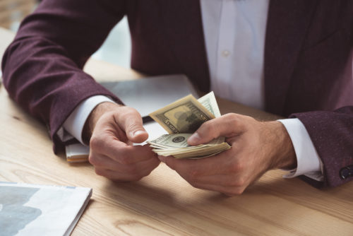 A closeup photo of a person in a maroon suit counting cash in their hands.