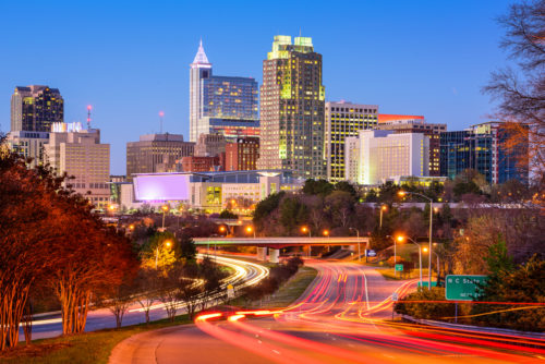 A long exposure photograph of the skyline and highway of Raleigh, North Carolina, with a deep blue sky.