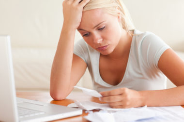 An image of a woman looking stressed out as she reads a receipt and has her laptop open.