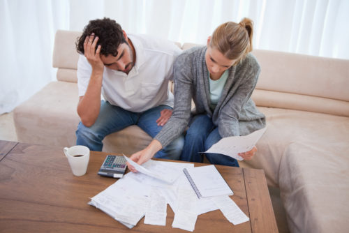 An image of a frustrated couple looking over many bills spread across their coffee table.