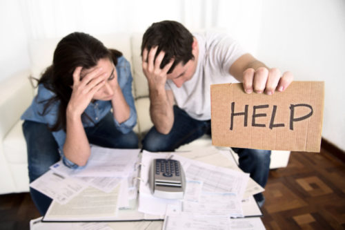 An image of a frustrated couple looking over debt papers, with the man holding up a sign that says "help."
