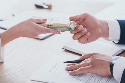 A man hands a woman a stack of money while touching a contract with his other hand.