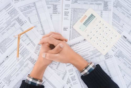 A man folds his hands together overtop a pile of tax forms with a calculator and a broken pencil.