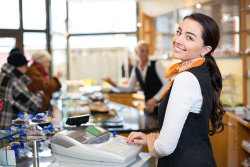 Salesperson working at a checkout counter in a busy shop, looking over her shoulder.