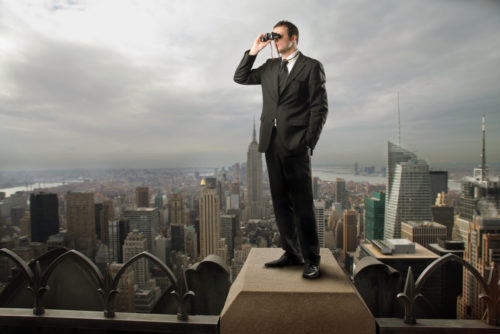 Man with binoculars on top of a building looking out over the city.