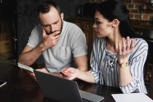 Stressed young couple with laptop and calculator counting credit debt