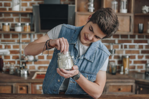 An image showing a young person placing money into a glass jar for savings.