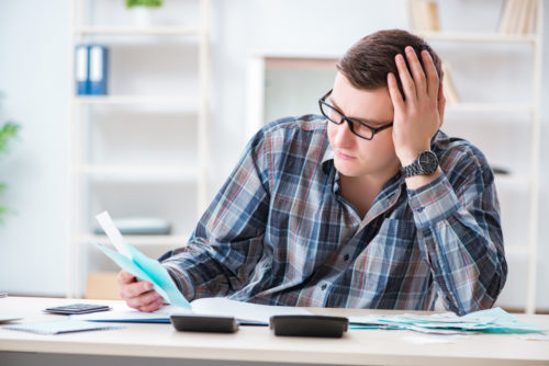 A man with his head in his hand, looking over some debt papers.